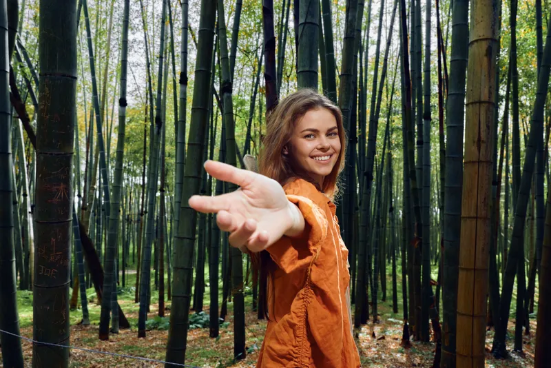 woman smile bamboo forest hand nature portrait outstretched, happy young woman leads the viewer by the hand through a sunlit bamboo grove wearing an orange shirt, outdoor lifestyle moment