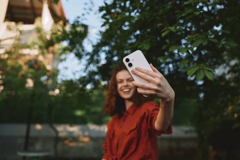 Woman lifestyle selfie outdoors smartphone red shirt smiling garden casual portrait cheerful fashion outdoor relax sunshine nature people girl youth summer leisure vibrant green background image