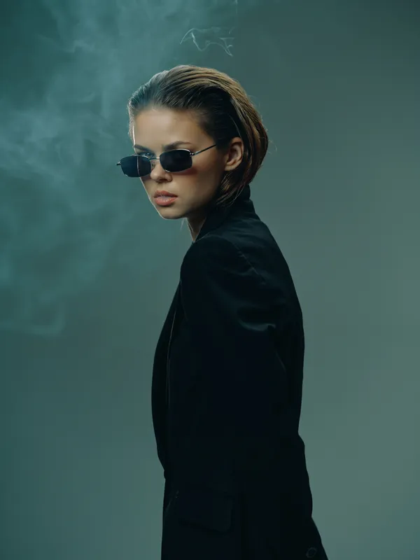Stylish woman in sunglasses and black jacket with moody smoke background and cool expression