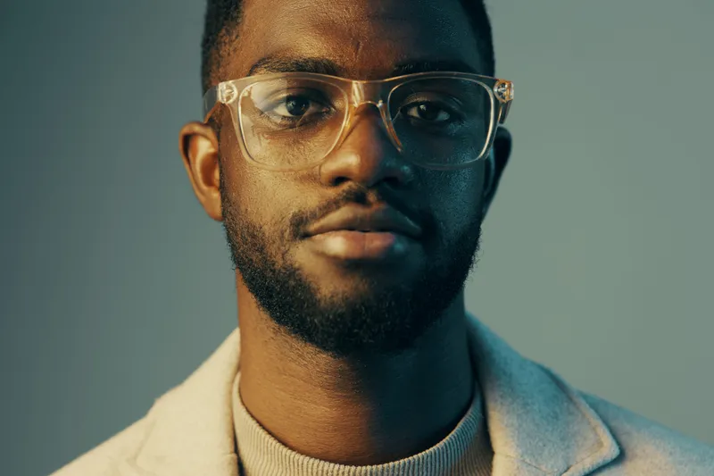 Stylish young man with glasses in a soft blue background, expressing confidence and modern elegance, perfect for portraits showcasing professionalism and contemporary style