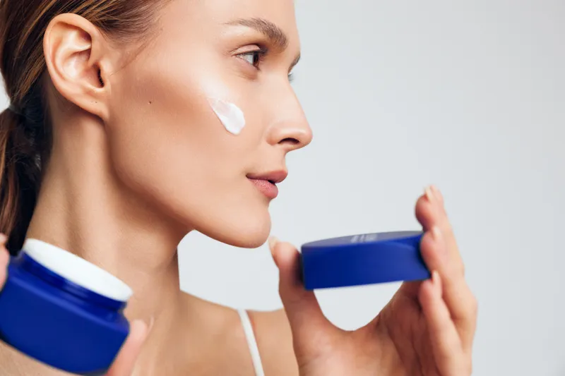 Close-up of a woman applying cream to her cheek, showcasing smooth skin, soft lighting, and a calm, focused moment during a skincare routine