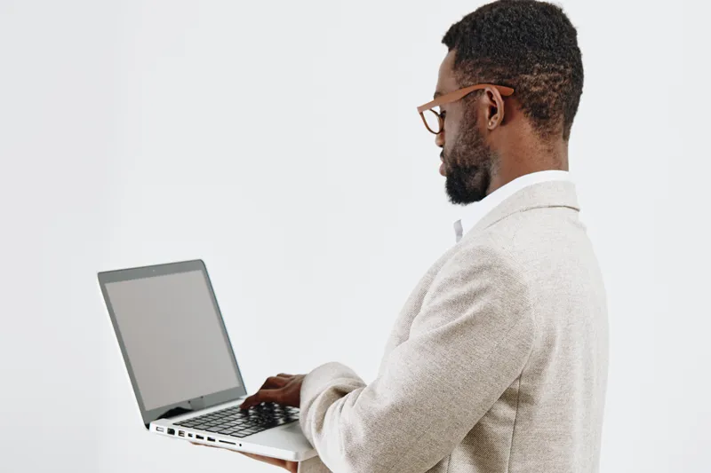 Professional man using laptop computer in bright office setting, dressed in smart casual blazer, focused on work, with beard and glasses, natural light, modern workspace, technology, business concept,
