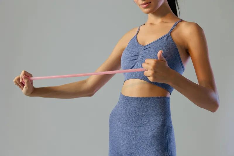 Woman sport fitness exercising with resistance band, wearing blue athletic clothing, stretching muscles, focused and active workout session indoors.