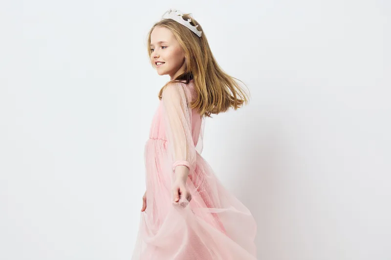 A joyful little girl in a pink dress with a tiara twirls gracefully against a soft, white background, exuding innocence and happiness