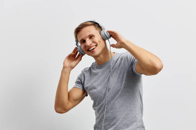 Smiling man wearing casual gray t-shirt listening to headphones, cheerful expression, enjoying music, white background, studio shot, lifestyle concept, happy and relaxed mood.
