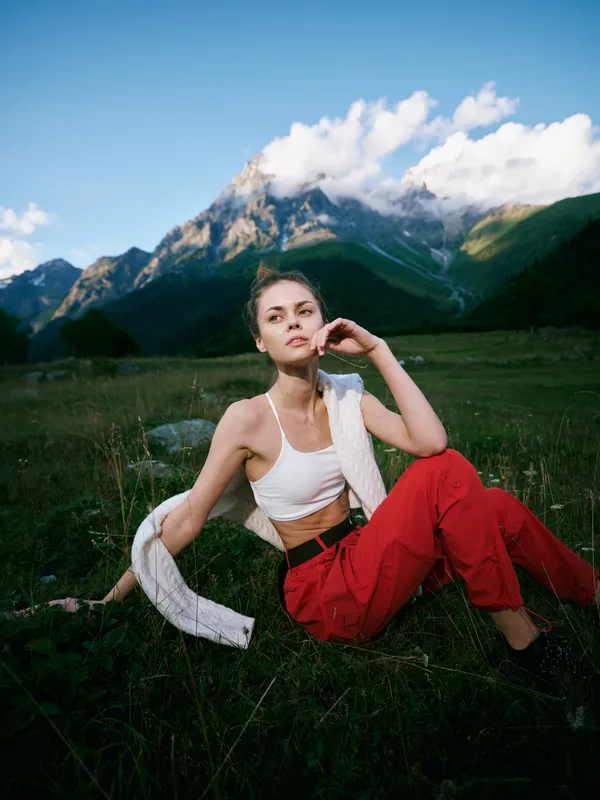 Mountain landscape outdoor female casual fashion field sky clouds nature scene with a relaxed vibe, a white crop top and red trousers, scarf draped over shoulder in a serene open air setting