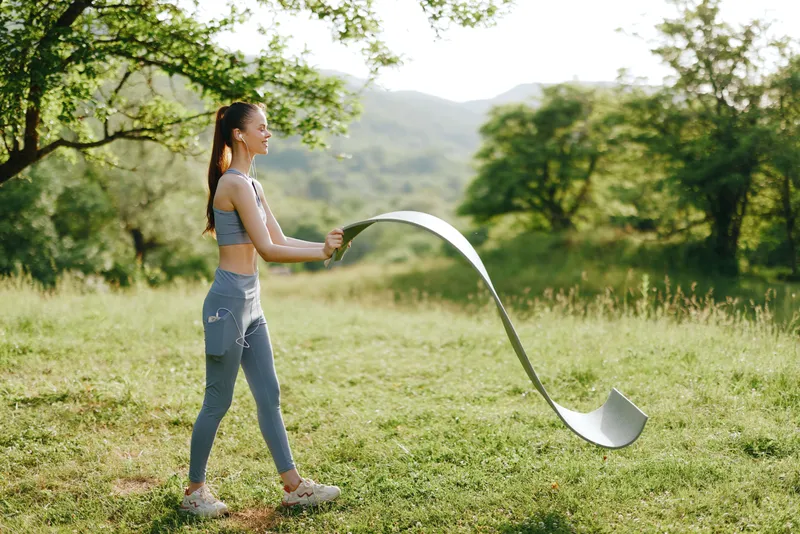 Young athletic woman practicing outdoor fitness with a flexible ribbon in a scenic green landscape, emphasizing health, motion, and vitality in nature