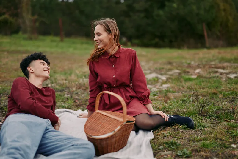 Young couple enjoying a genuine outdoor picnic on a blanket, captured with authentic relaxed expressions and natural interaction, conveying credibility, warmth and a sincere emotional connection.