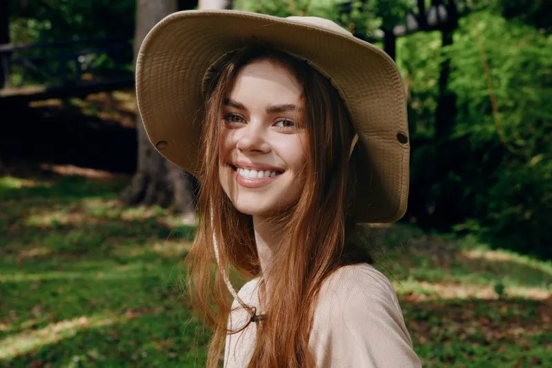 Woman smile hat portrait outdoor nature happy hair, young female wearing sunhat in green park, closeup face with natural sunlight, cheerful relaxed summer mood and casual style.