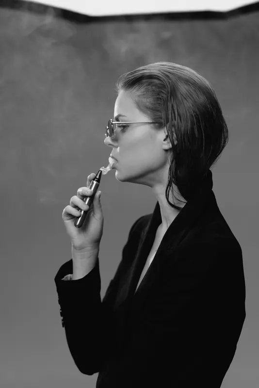Black and white portrait of a thoughtful woman in glasses holding a vape device