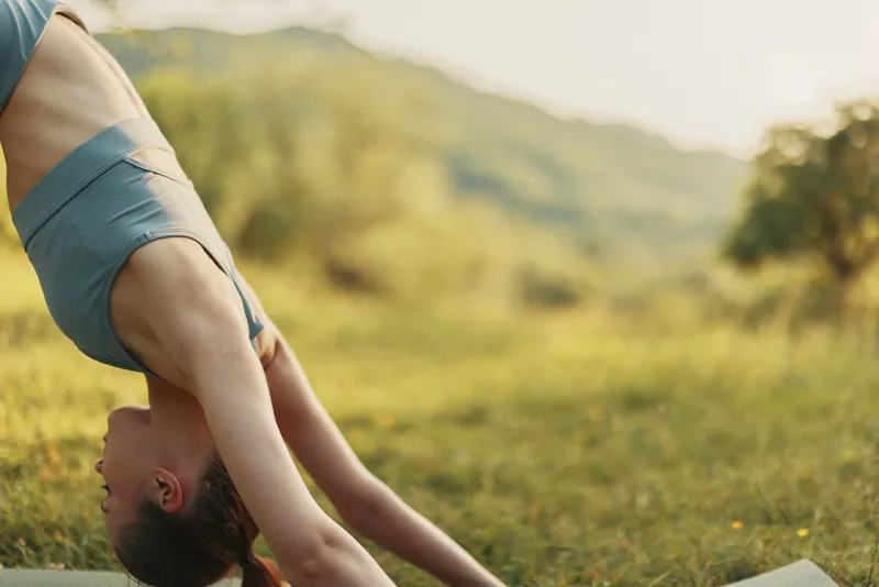 A young model performing a downward dog yoga pose in a scenic outdoor location, showcasing a healthy lifestyle and connection with nature