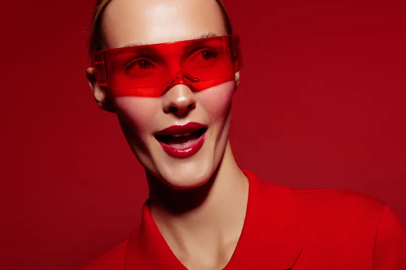 Portrait of a fashionable woman wearing red sunglasses and red lipstick against a red background. Concept of style, fashion, beauty, and modern accessories in studio lighting.