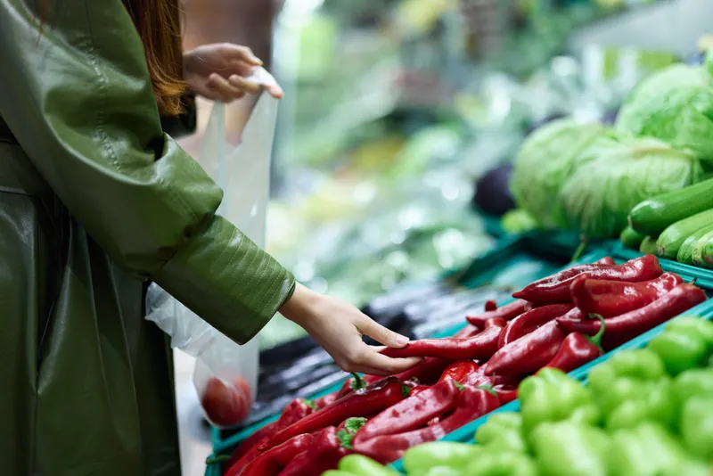 Женщина в продуктовом магазине выбирает свежие овощи для приготовления ужина дома