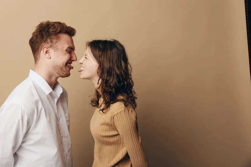 Happy young couple smiling and leaning close to each other against beige background. Concept of love, relationship, intimacy, and positive emotions between man and woman.
