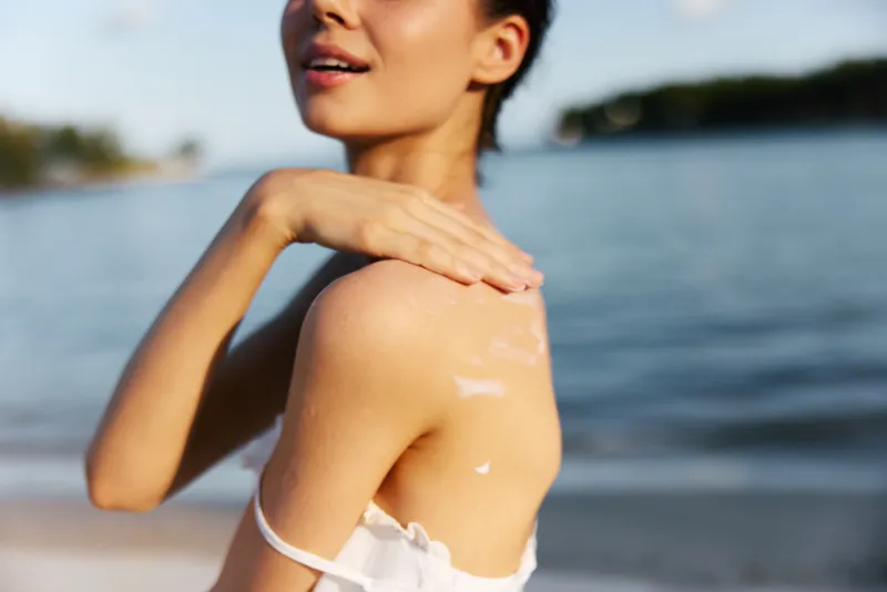 Close up of sunlit shoulder and neck of a woman at the seaside, sunscreen on skin, soft breeze, warm light, relaxed mood.