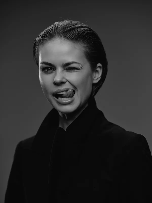 Portrait of a playful woman winking and sticking out her tongue in black and white with a dark background.