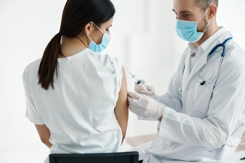 Врач в медицинской маске делает инъекцию вакцины в плечо женщины в инфекционной больнице