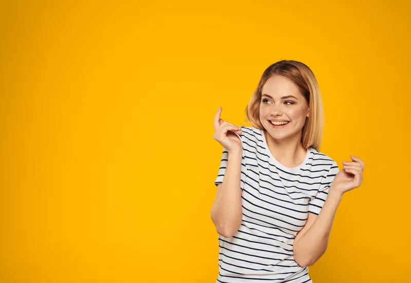 Счастливая блондинка на жёлтом фоне жестикулирует руками и смеётся от радости