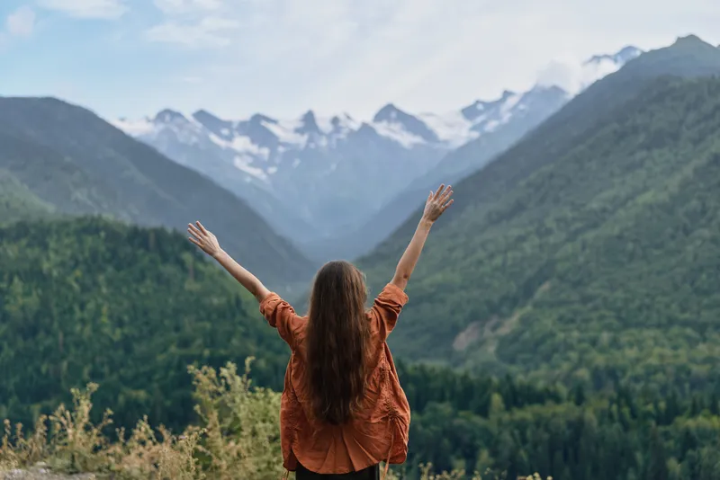 Person with arms raised in mountains nature and valley feeling freedom authenticity inclusivity outdoor landscape