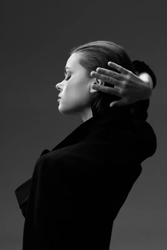 Elegant woman in black coat posing in black and white fine art portrait with dramatic lighting and thoughtful expression