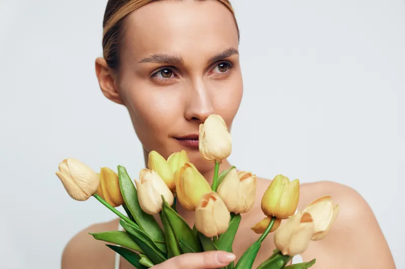 Woman holding a bouquet of tulips, close up portrait, beauty and skincare concept, soft studio light, spring wellness mood, calm expression, minimal background