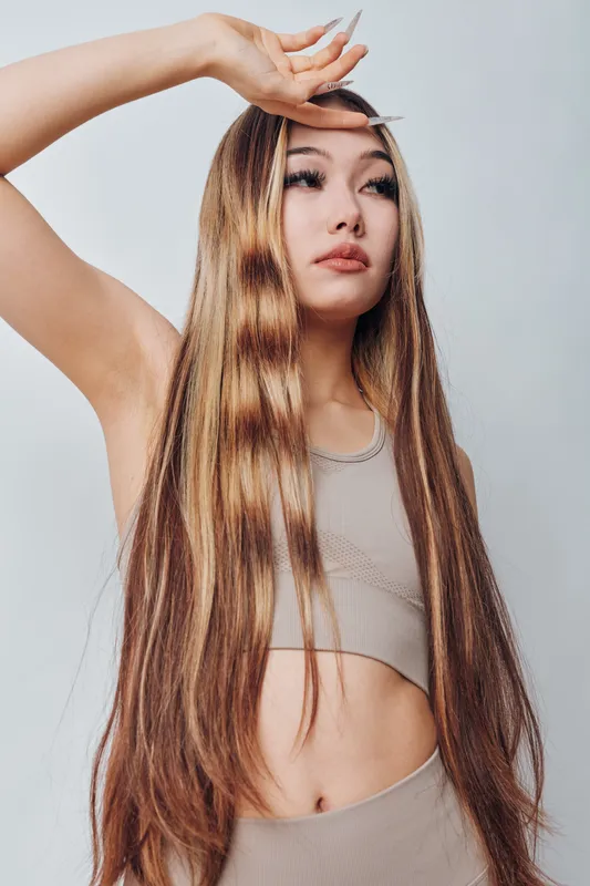 Woman with long straight hair wearing sleeveless top posing with hand near forehead isolated on white background. Beauty model with natural makeup and casual outfit.