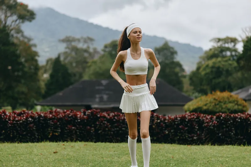 Young athletic woman jogging in a white sports outfit, showcasing determination and fitness against a scenic outdoor backdrop
