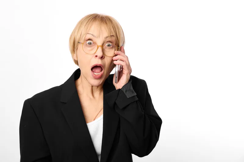 Surprised older woman in blazer, holding phone to her ear, call and communication, shocked portrait in studio, white background, soft light, for customer support