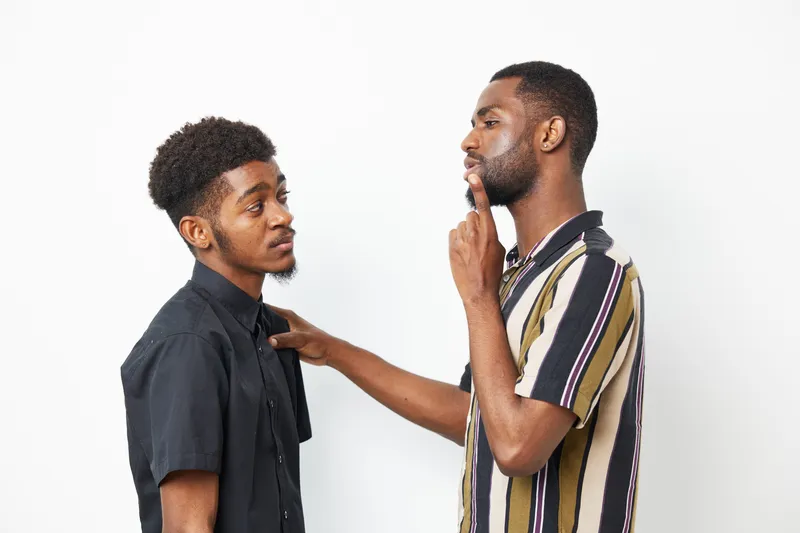 Two African American men engaged in a thoughtful discussion, showcasing friendship and connection. The casual attire complements their expressive facial features.