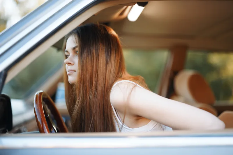 Young woman with long hair sitting in a car, looking thoughtful, representing a moment of reflection and tranquility.