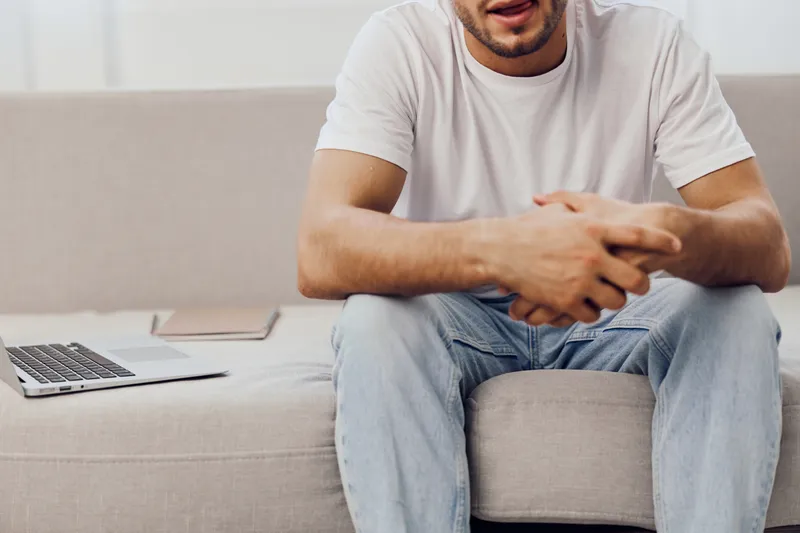 Casual man sitting on a couch, expressing contemplation with a relaxed demeanor, surrounded by a tidy workspace, promoting productivity and modern living.