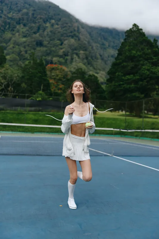 Young woman enjoying a healthy lifestyle on a tennis court, wearing sporty attire, surrounded by nature, radiating joy and vitality