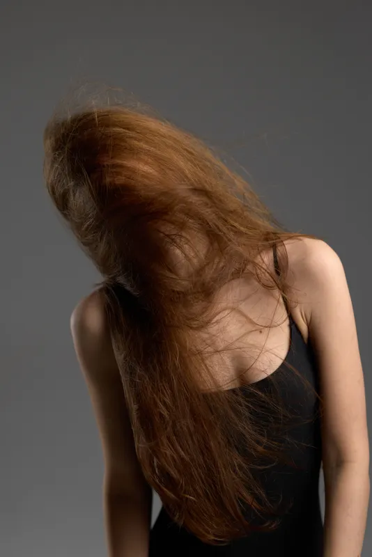 Woman with long brown hair in black top moving her hair indoors, neutral background, dynamic and stylish portrait