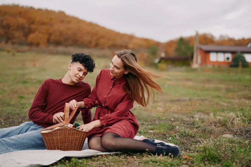 A candid young couple sharing a picnic on a rustic meadow, genuine interaction and relaxed smiles captured naturally to convey authenticity and credibility in an everyday connection.