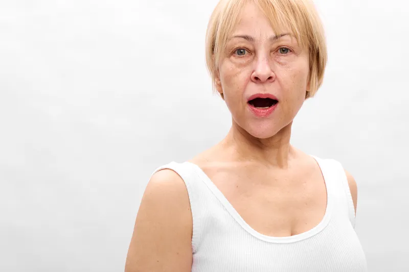 Blonde woman portrait with surprise and shocked expression, mouth open in shock, eyes widened on a white studio background, isolated concept emotion.