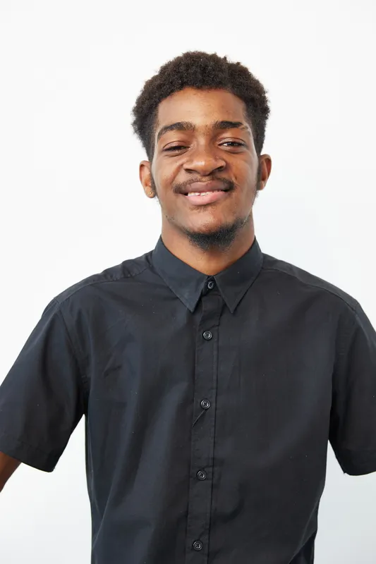 Black man smiling confidently against a clean white background, showcasing joy and positivity in a casual, stylish outfit. Perfect for uplifting content.