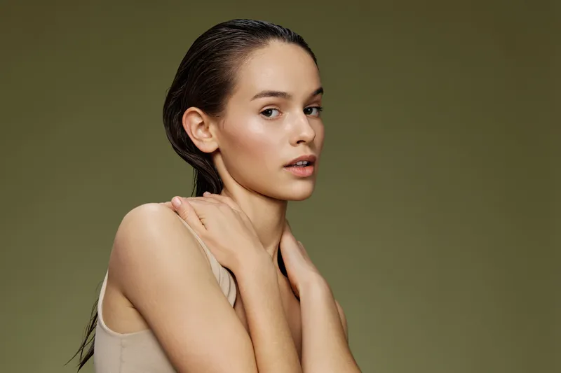 Young model with wet hair posing against a soft green background, radiating natural beauty and confidence Emphasizes concepts of skincare and fresh looks