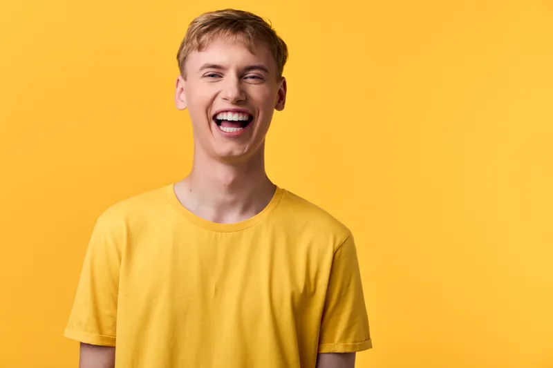 Smiling man in a yellow tee stands against a vibrant yellow backdrop, radiating cheerfulness, optimism, and sunny energy ideal for lifestyle, fashion, and positivity campaigns.