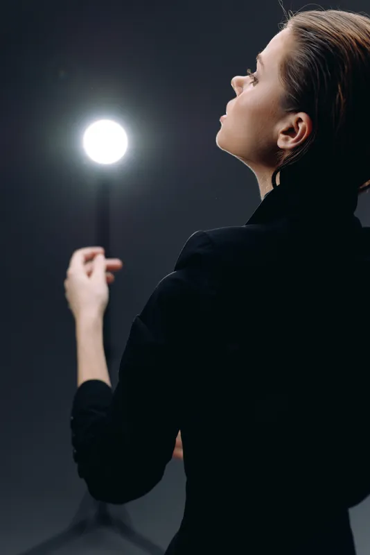 woman in black dress facing bright studio light on dark background, artistic concept with dramatic mood