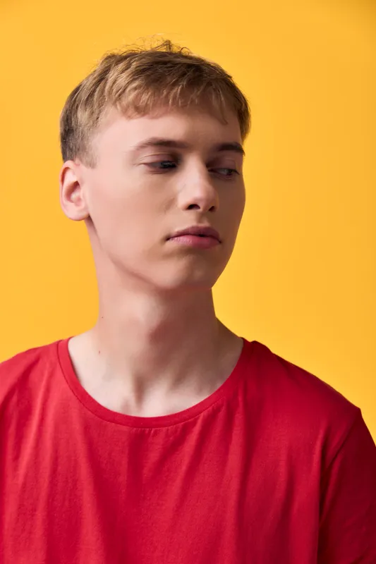 Young man in a casual red shirt against a yellow background, side profile and thoughtful expression, studio shot emphasizing color and mood for fashion or lifestyle stock
