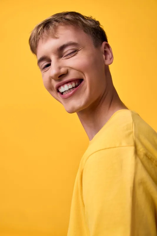 Smile and happiness shine from a joyful man in a casual studio headshot, wearing a yellow shirt against a bright background, conveying warm, modern lifestyle and positive energy