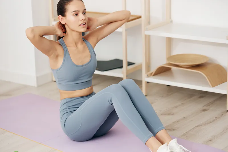 Young woman fitness scene doing sit ups on a pastel yoga mat in a bright minimalist living room, wearing matching athletic set and sneakers, focused on core training at home