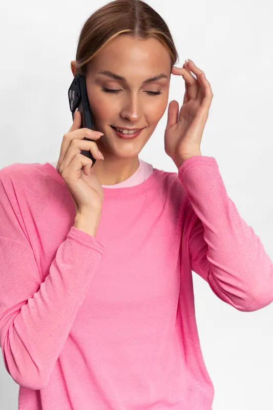 Young woman in pink sweater smiling and talking on smartphone, enjoying conversation. Indoor studio portrait with white background, casual lifestyle and communication concept.