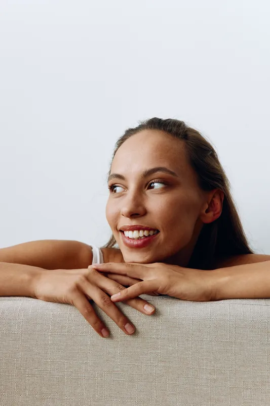Портрет молодой женщины с загорелой кожей и красивой улыбкой с белыми зубами, лежащей с опорой на руки