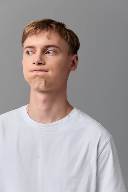 Man with a pout wearing a white tee shirt, looking to the side against a gray background, casual lifestyle image with humorous, relaxed vibe.