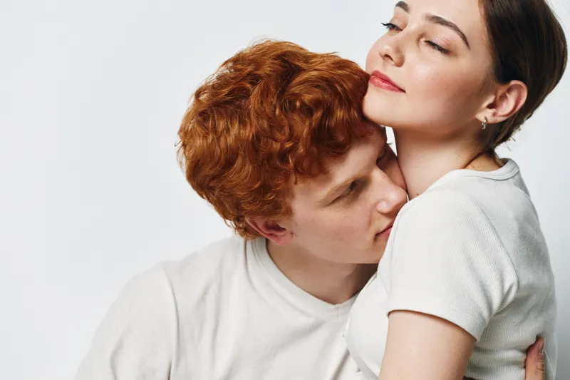 Couple embracing and sharing tender moment with closed eyes in white clothes on light background. Young man and woman with affection and intimacy for love and connection.