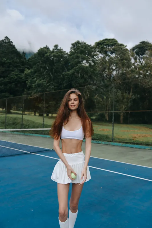 Young athletic woman in sporty outfit plays tennis on outdoor court, showcasing joyful emotions with vibrant colors and natural background