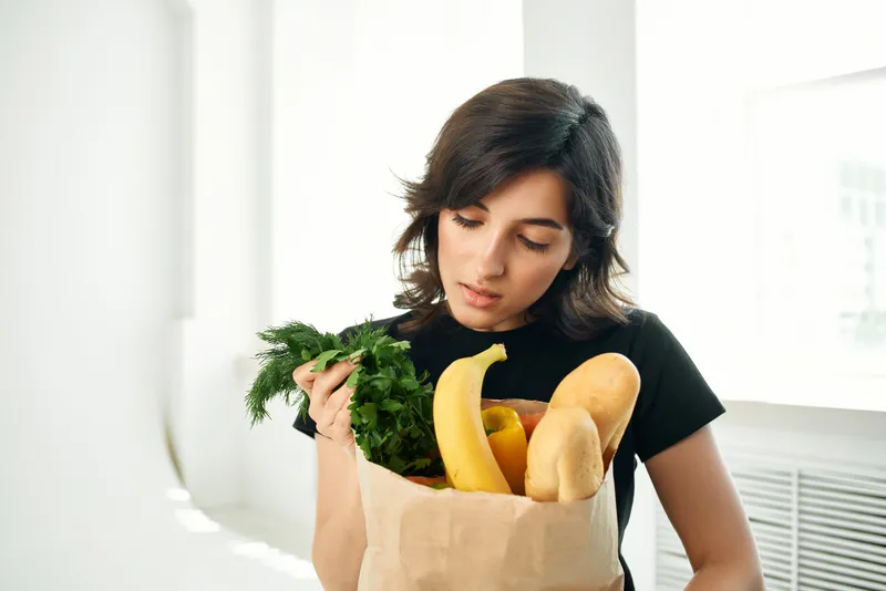 Брюнетка с пакетом продуктов готовит здоровую еду на доставку