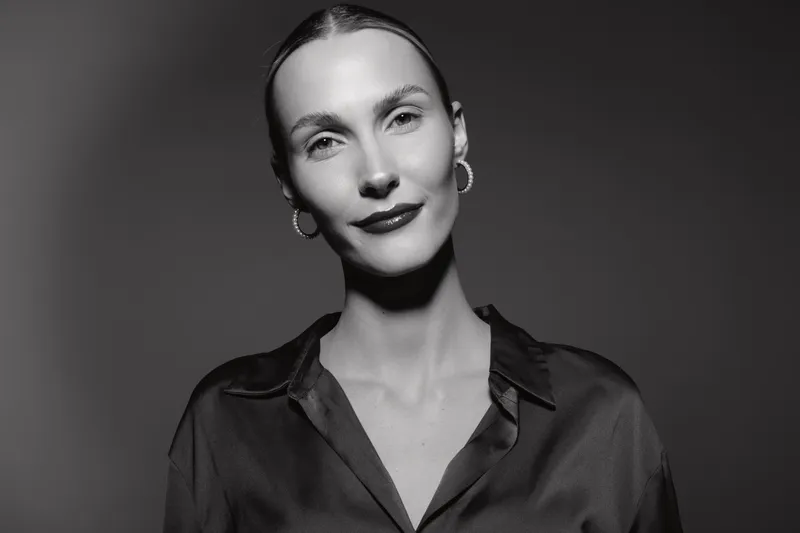 Portrait of a young white woman with fair skin smiling confidently in a black shirt against a dark background. Concept for beauty, confidence, and elegance.