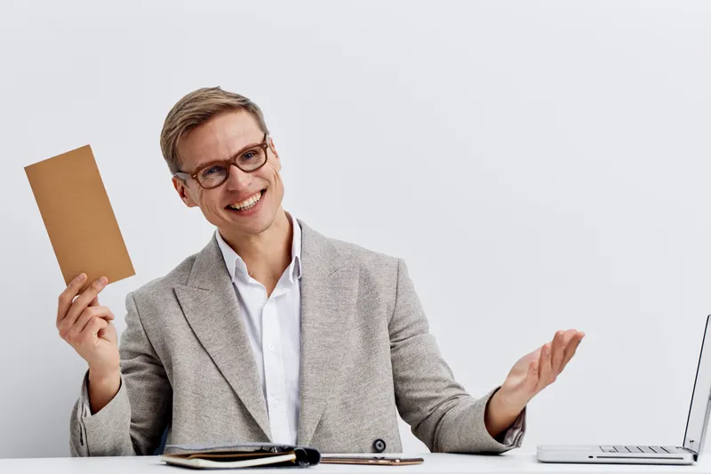 Smiling man in business suit holding notepad while sitting at desk with laptop isolated on plain white background studio portrait. Business, success, communication, confident, professional, modern sty